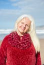 Elderly woman in red sweater smiling on a sunny beach in Portugal.